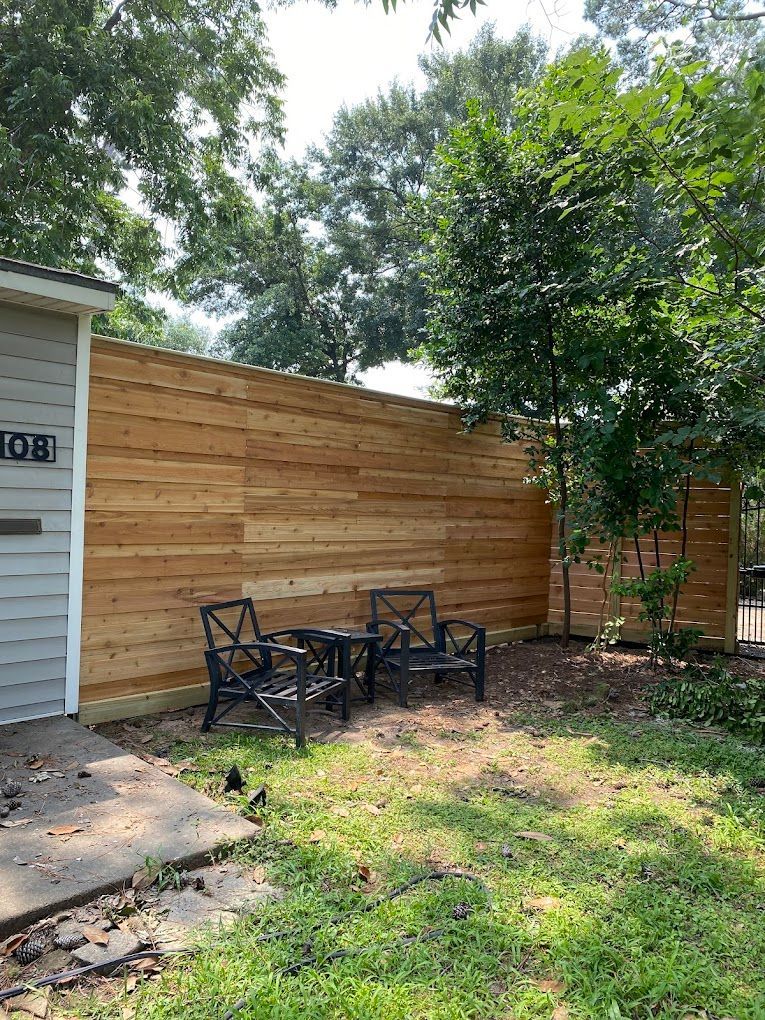 A wooden fence with chairs and a table in front of a garage.