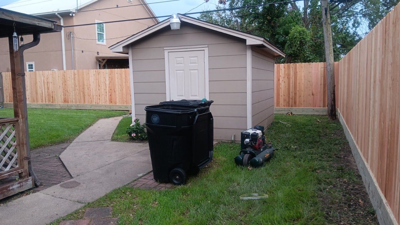 A backyard with a shed , trash cans and a wooden fence.