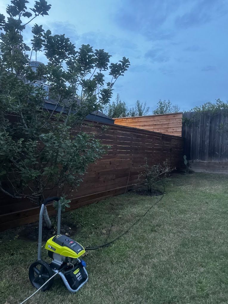 A pressure washer is sitting in the grass in front of a wooden fence.