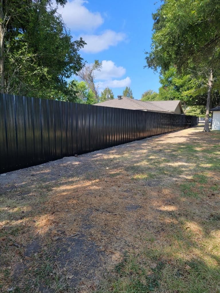 A long black fence surrounds a grassy yard in front of a house.