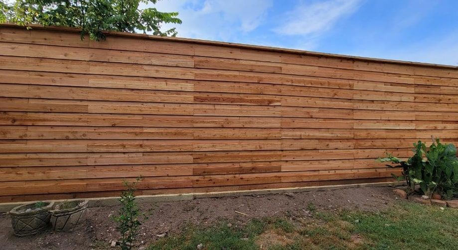 A wooden fence in a backyard with a blue sky in the background.