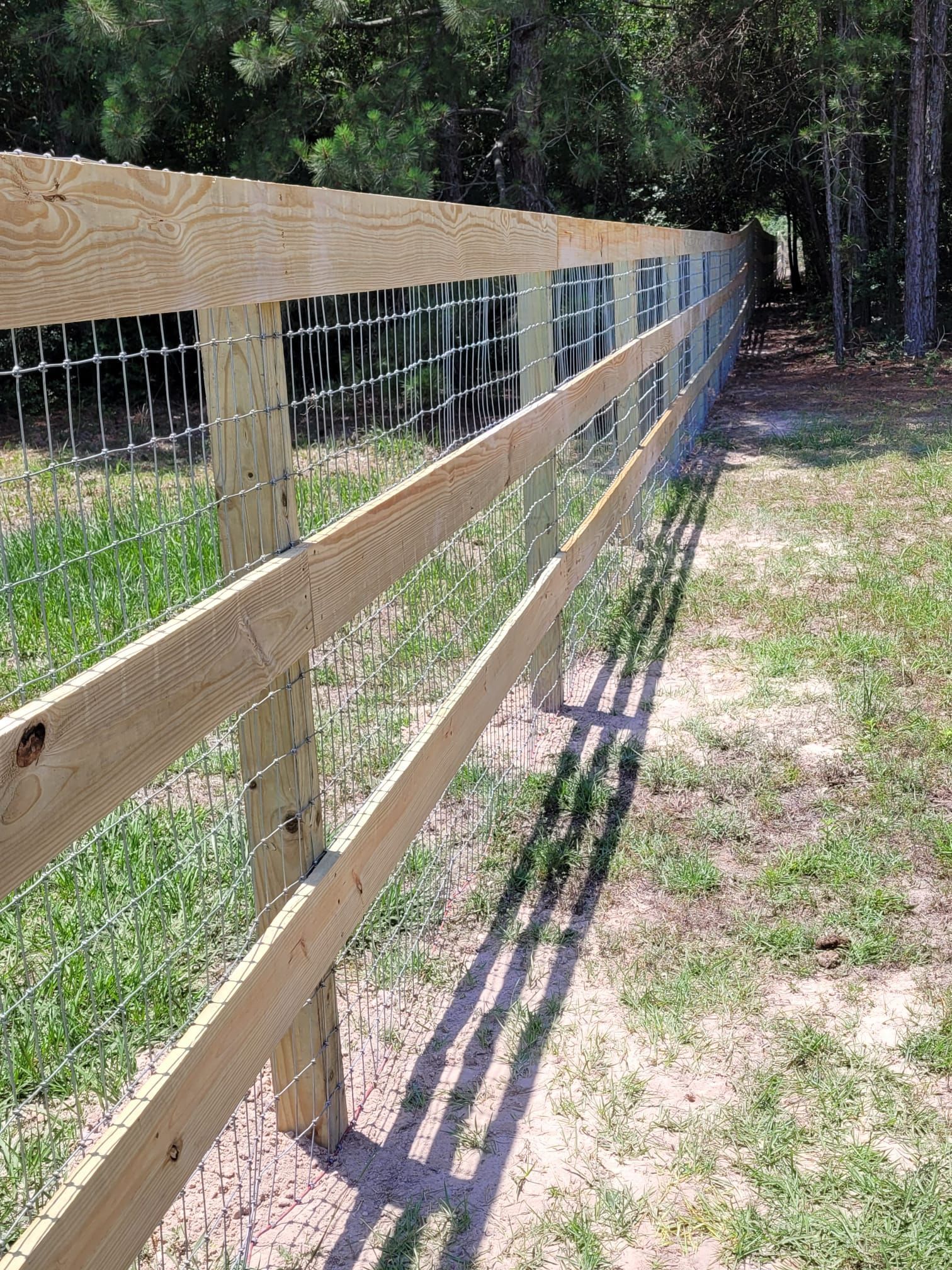 A wooden fence with a wire fence behind it in a grassy field.