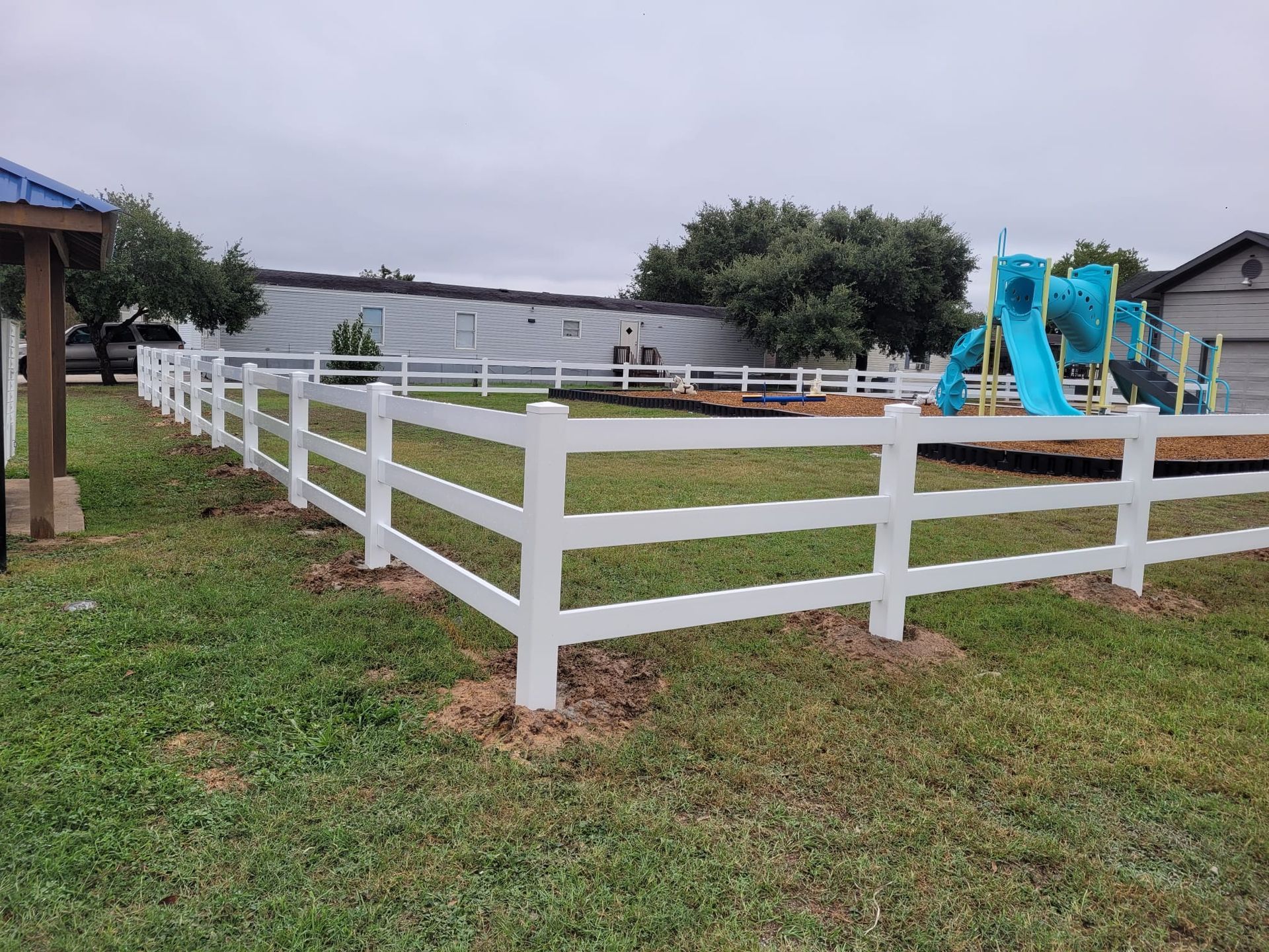 A white fence surrounds a playground in a yard.