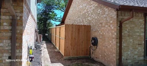 A wooden fence is being built on the side of a brick house.