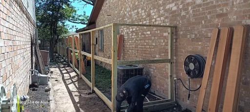 A man is working on a wooden fence next to a brick wall.