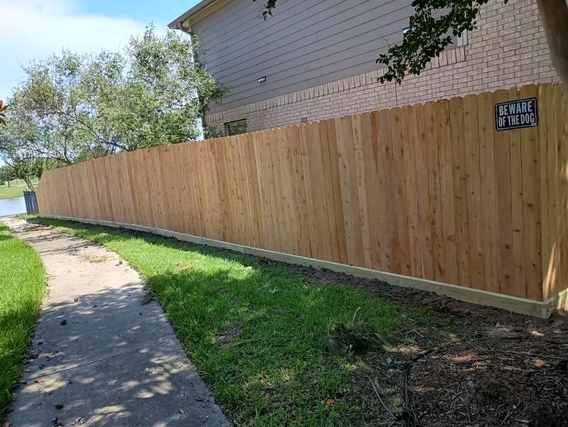 A wooden fence is sitting next to a sidewalk in front of a house.