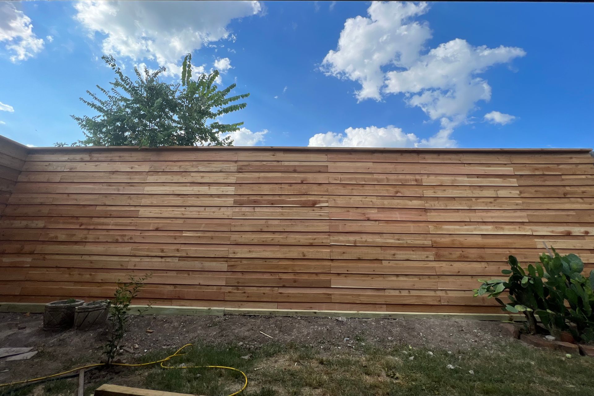 A wooden fence in a backyard with a blue sky in the background.