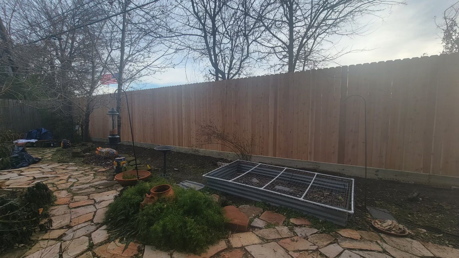 A wooden fence surrounds a stone patio in a backyard.