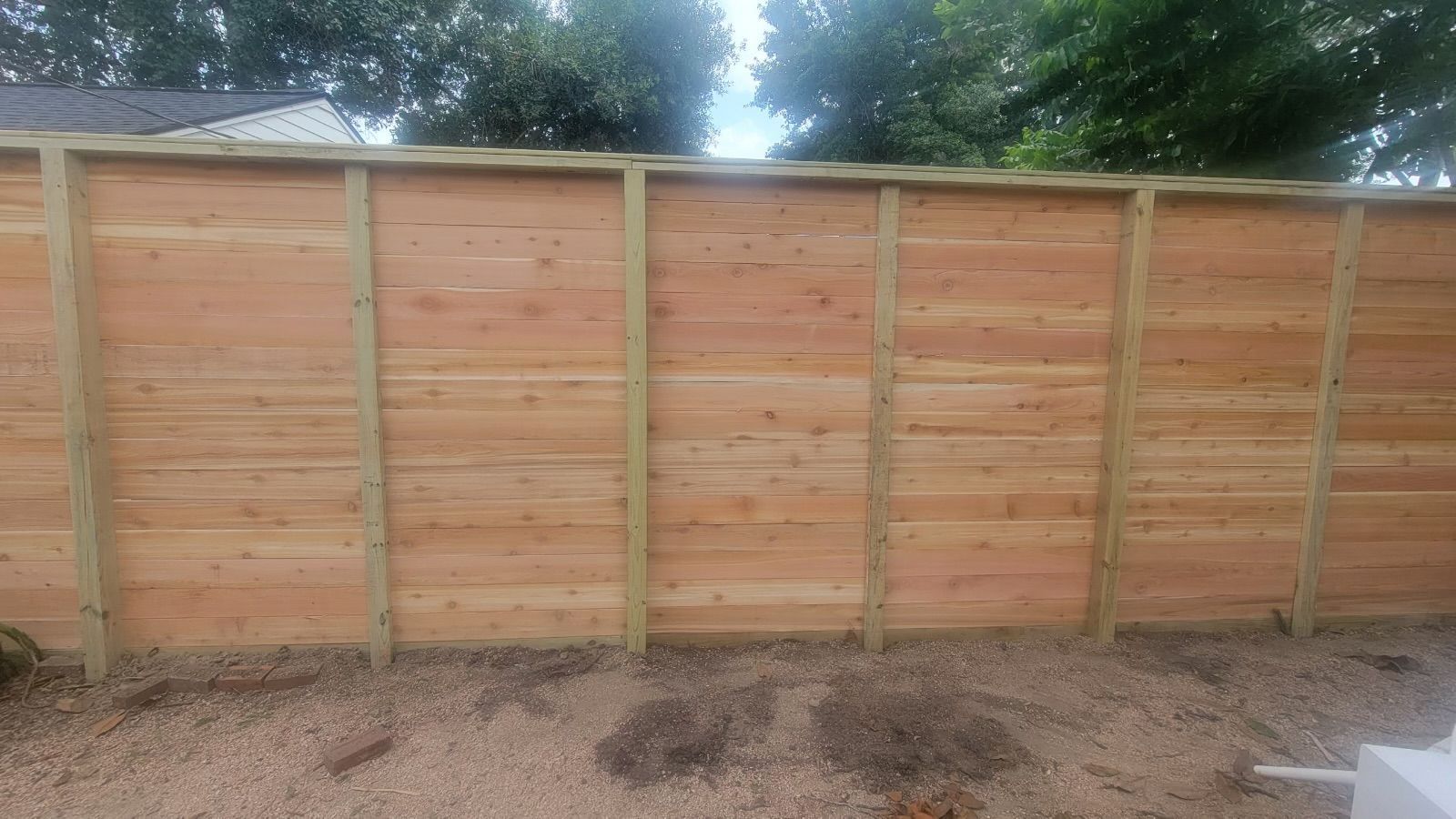 A wooden fence is sitting in the middle of a gravel yard.