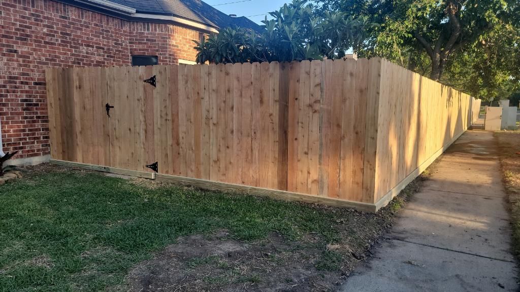 A wooden fence is sitting next to a sidewalk in front of a brick house.