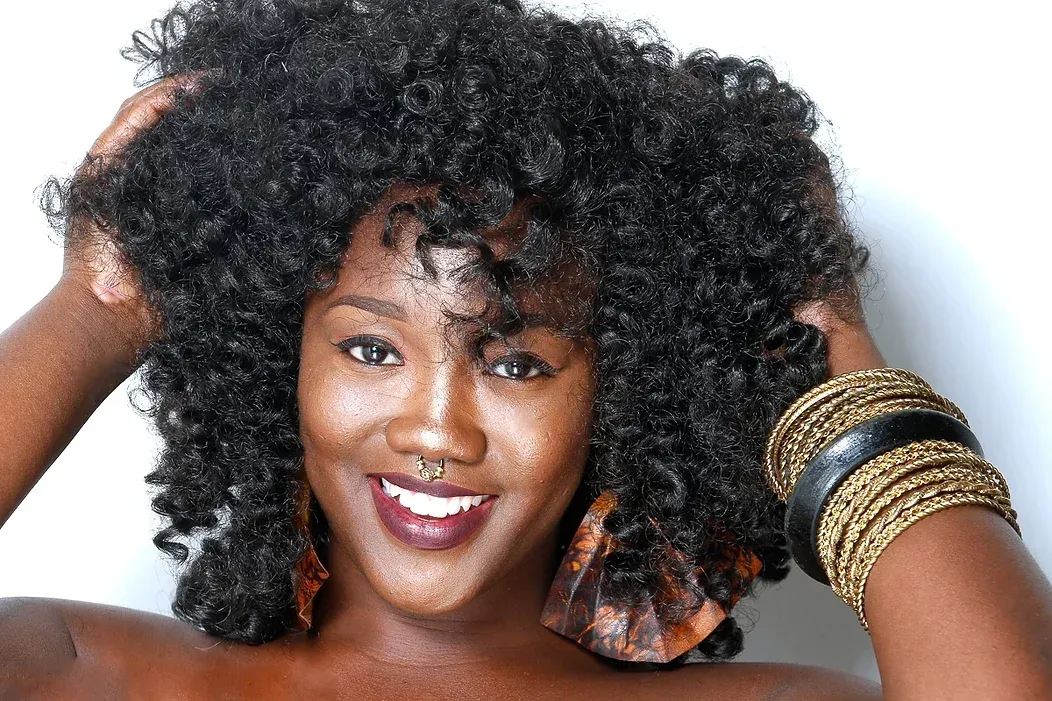 A woman with curly hair is smiling and holding her hair.