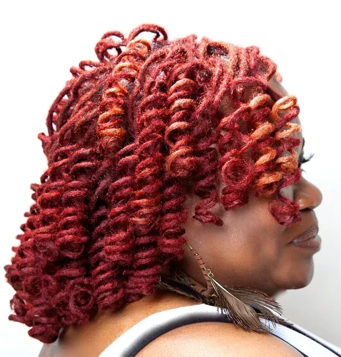 A woman with red curly hair is wearing a white tank top