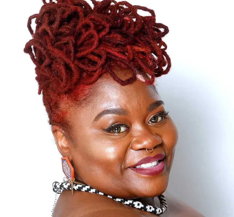 A woman with red dreadlocks is smiling and wearing a necklace