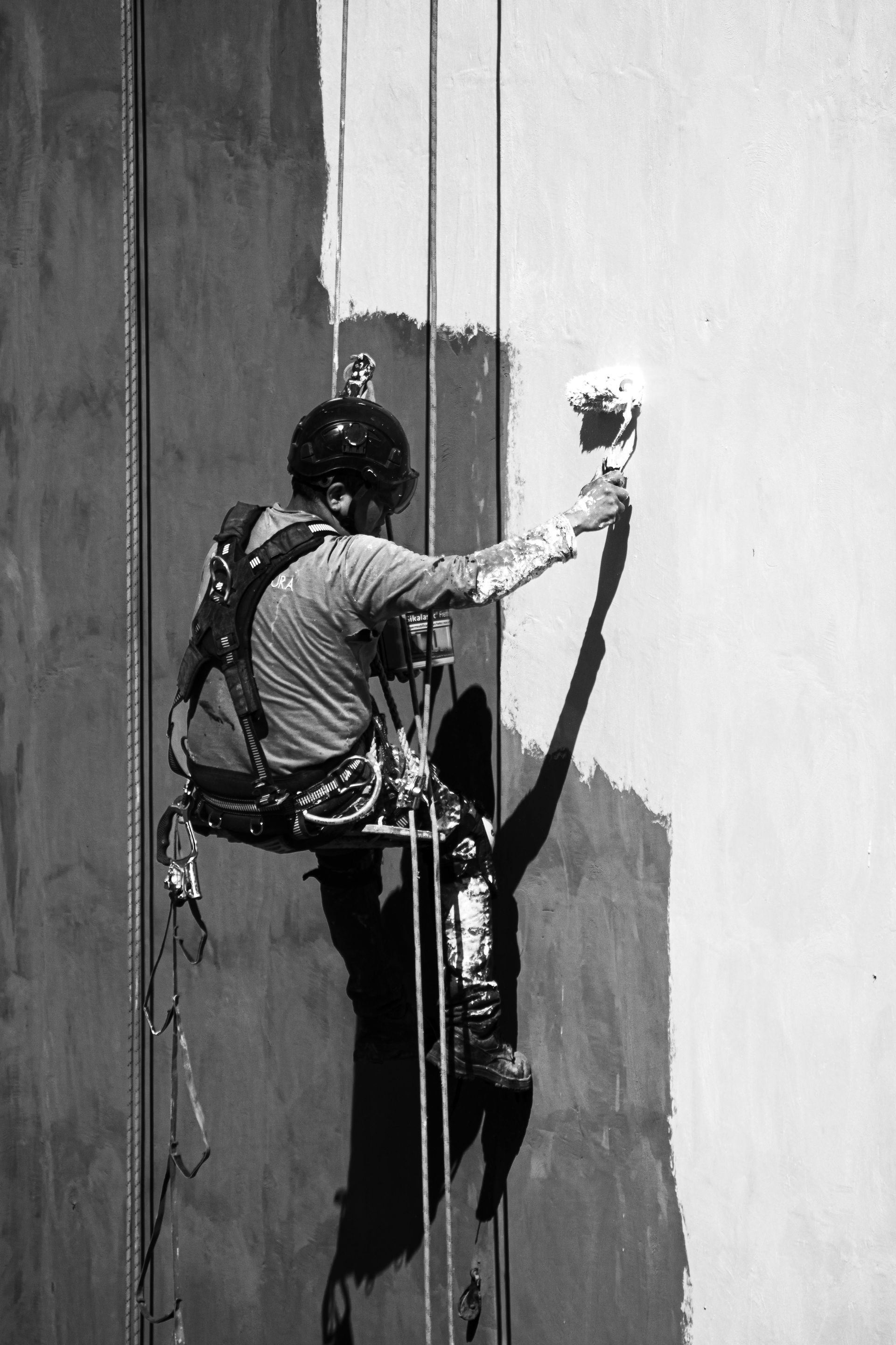 Painter suspended on ropes, applying paint to a high building wall.