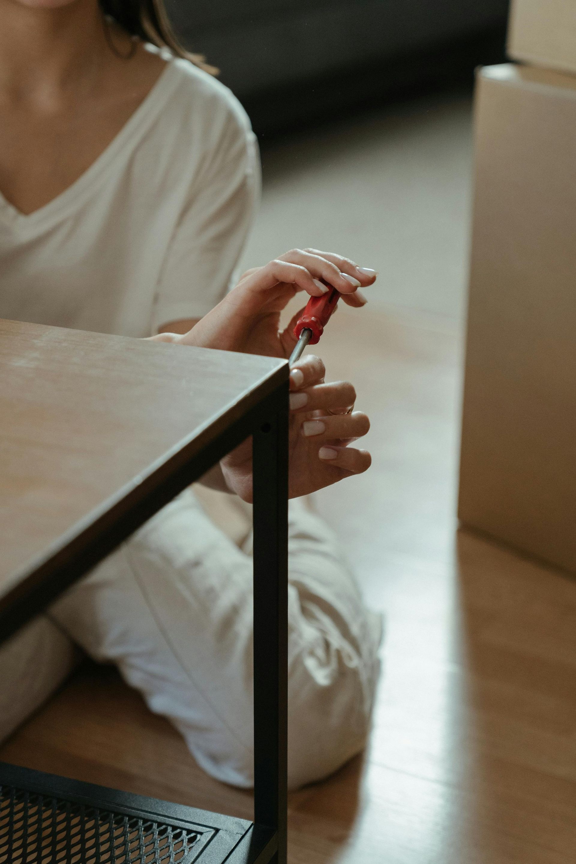Person assembling furniture with a red screwdriver, sitting on the floor.