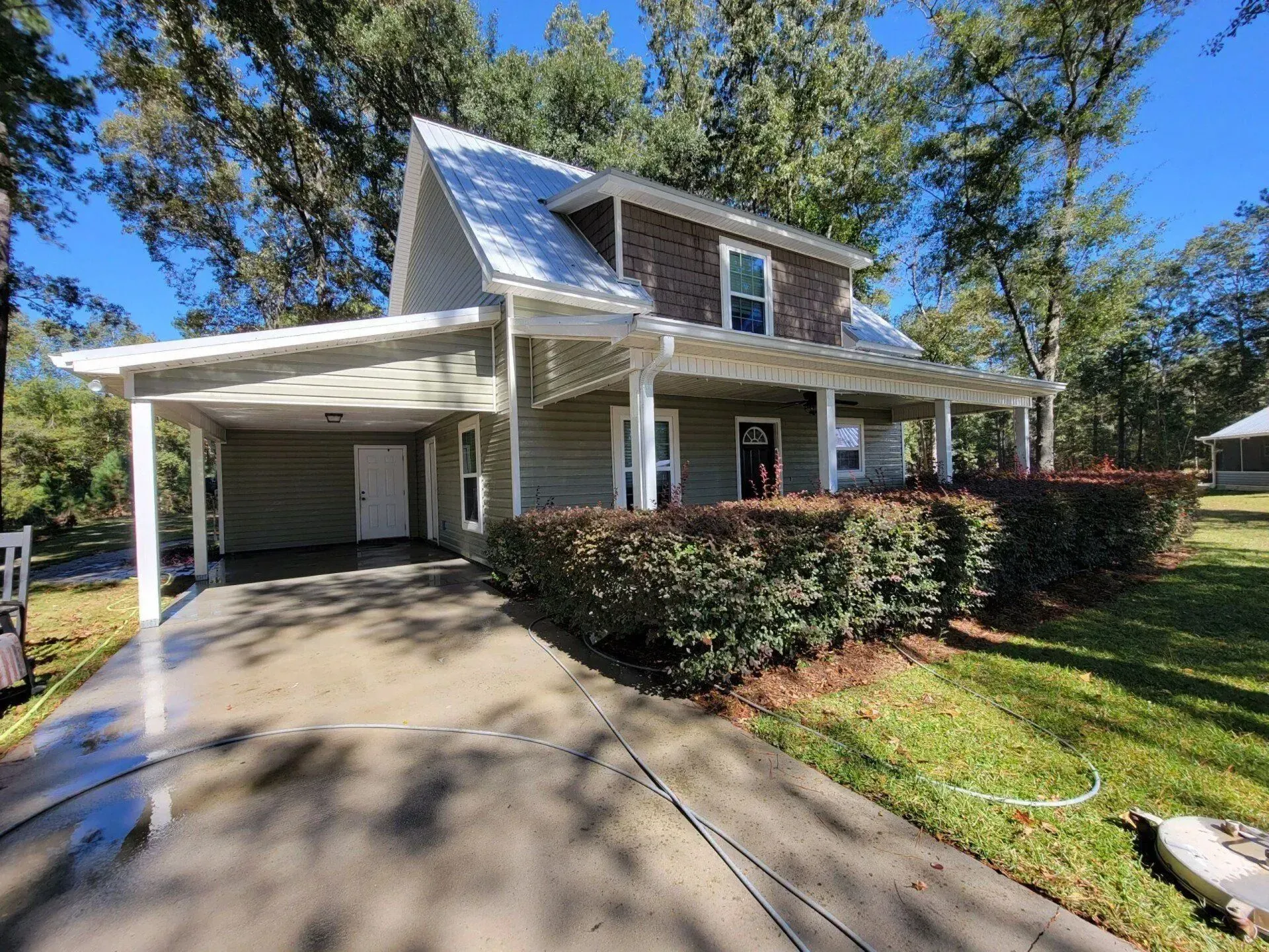 House with carport, covered porch, green siding, brown roof, and driveway.