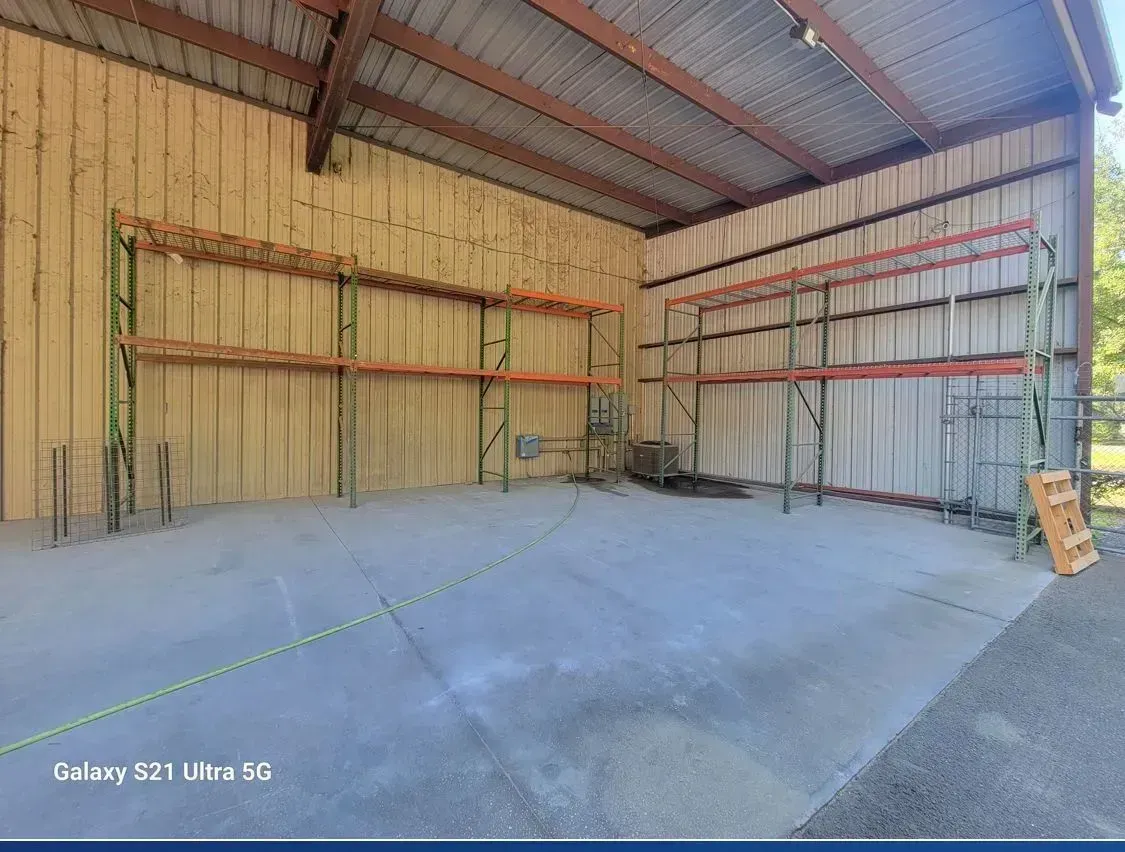 Interior of an empty warehouse with metal shelving on the walls. Gray concrete floor, corrugated metal walls and roof.