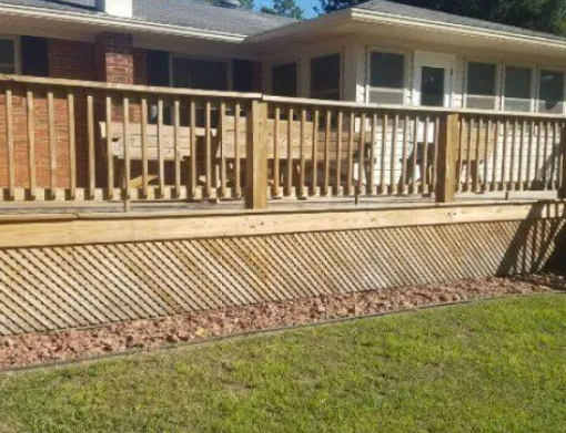 Wooden deck with lattice skirting, bordering a lawn with reddish stones.