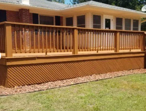 Wooden deck with lattice skirting and railing, painted brown, in front of a house on a grassy lawn.