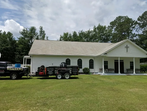 White church with a cross above the entrance and two trailers on the lawn in front.
