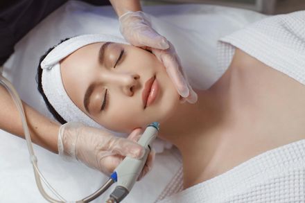Woman receiving a facial treatment, lying on a spa bed with gloved hands using a skincare device.