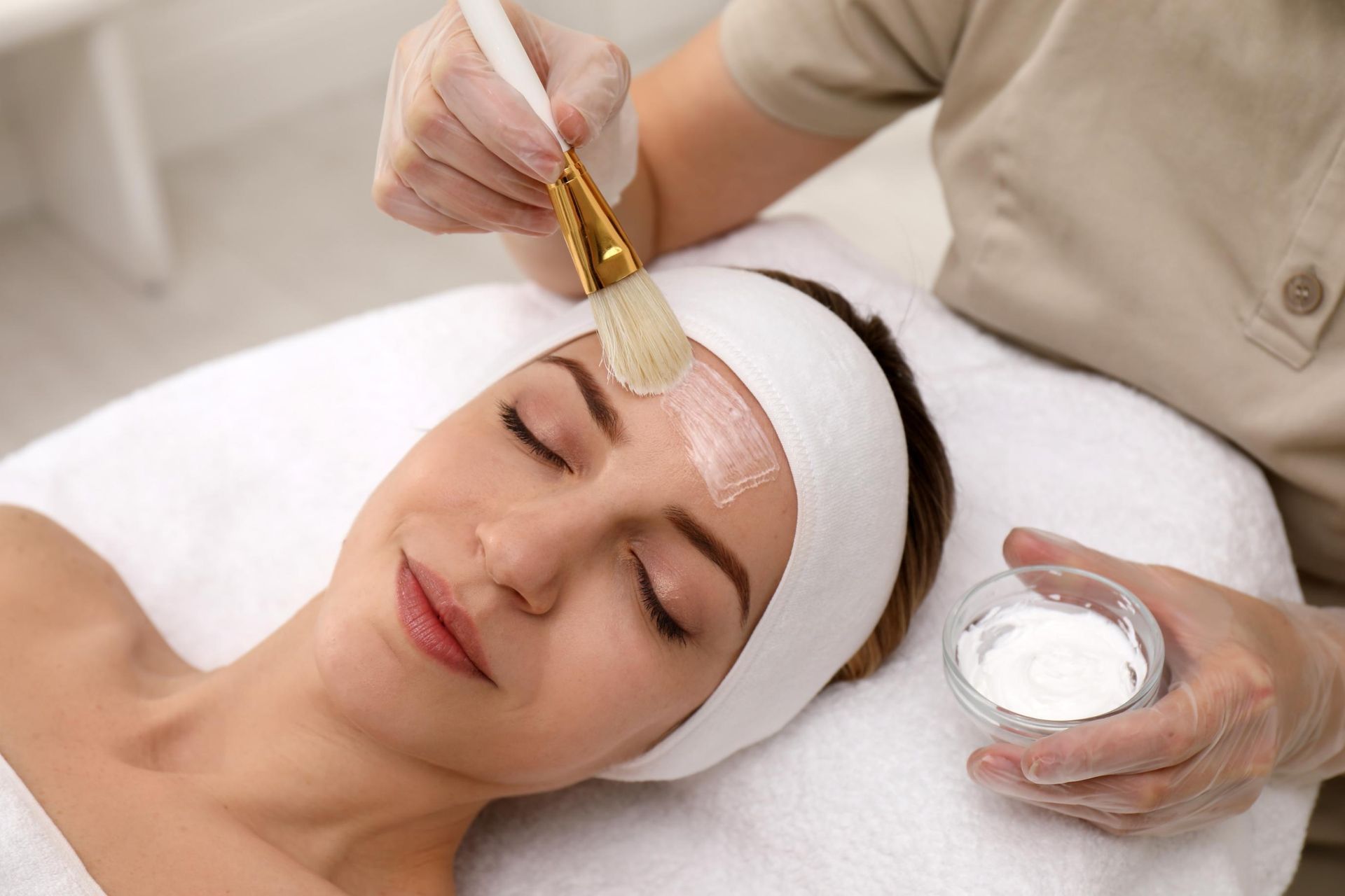 Spa facial treatment with a brush applying cream to a woman’s forehead