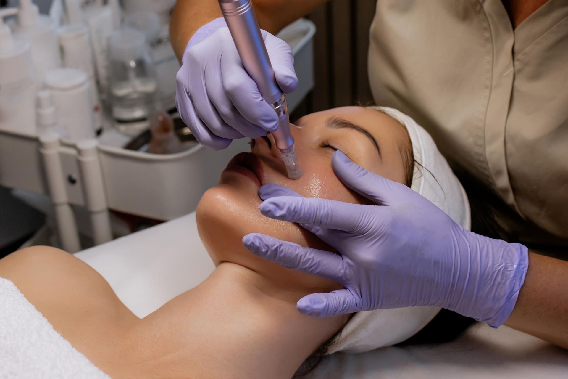 Cosmetic treatment on a person’s face with gloved hands using a handheld device in a clinic setting
