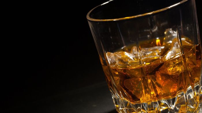 A lowball glass filled with amber-colored liquid and ice cubes, set against a dark background.
