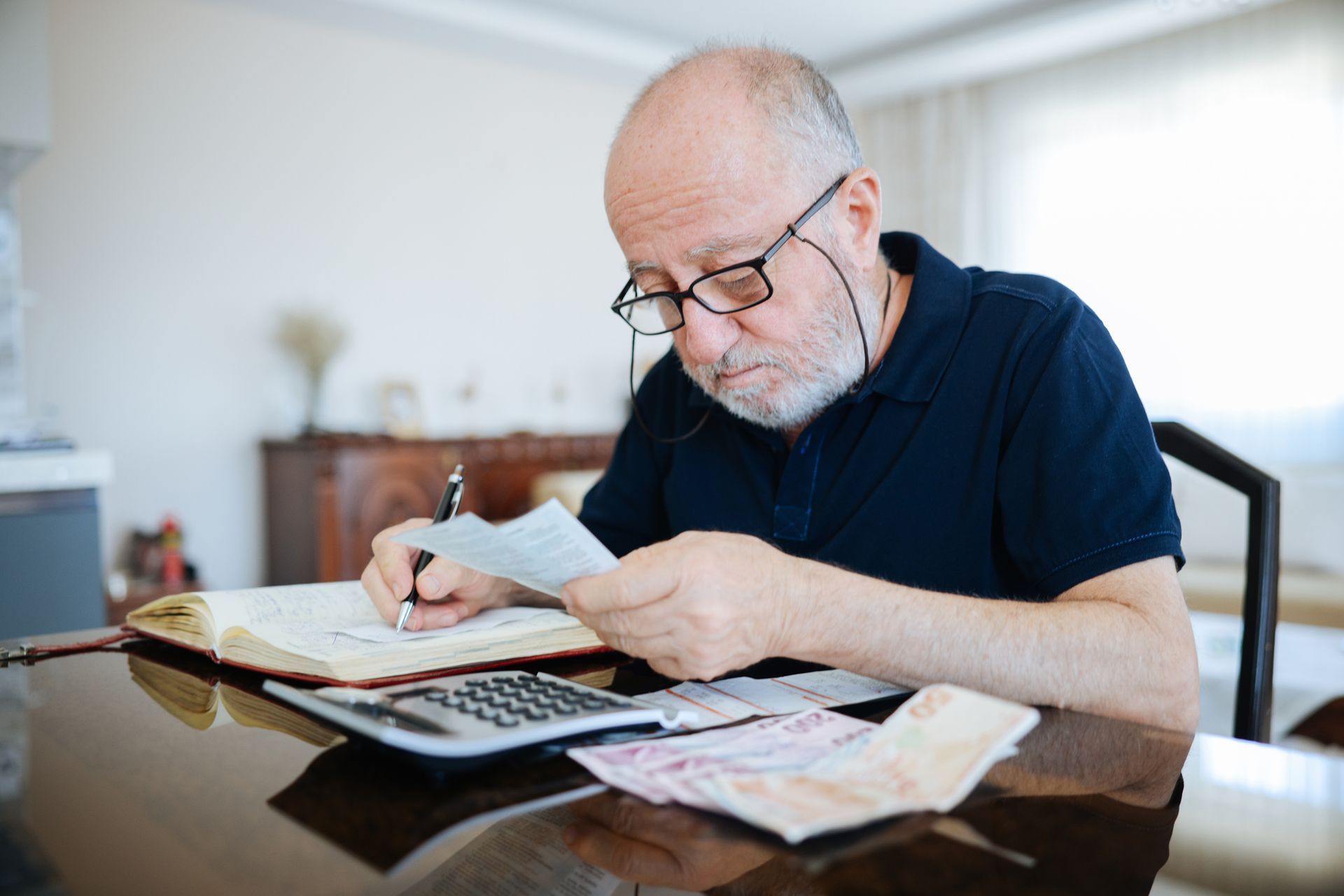 An anxious senior man managing finances, holding cash, and using a calculator at home. An anxious senior man managing finances, holding cash, and using a calculator at home.
