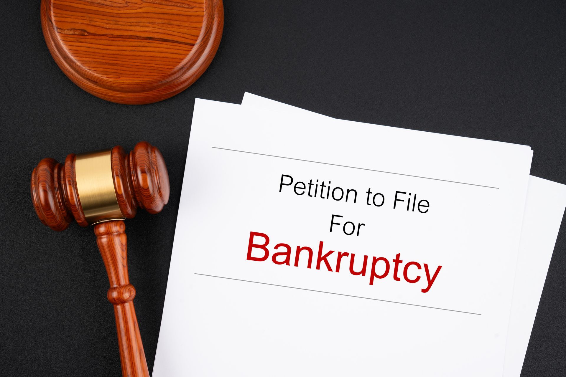 A bankruptcy document with a wooden judge's gavel on a black table. A bankruptcy document with a wooden judge's gavel on a black table.