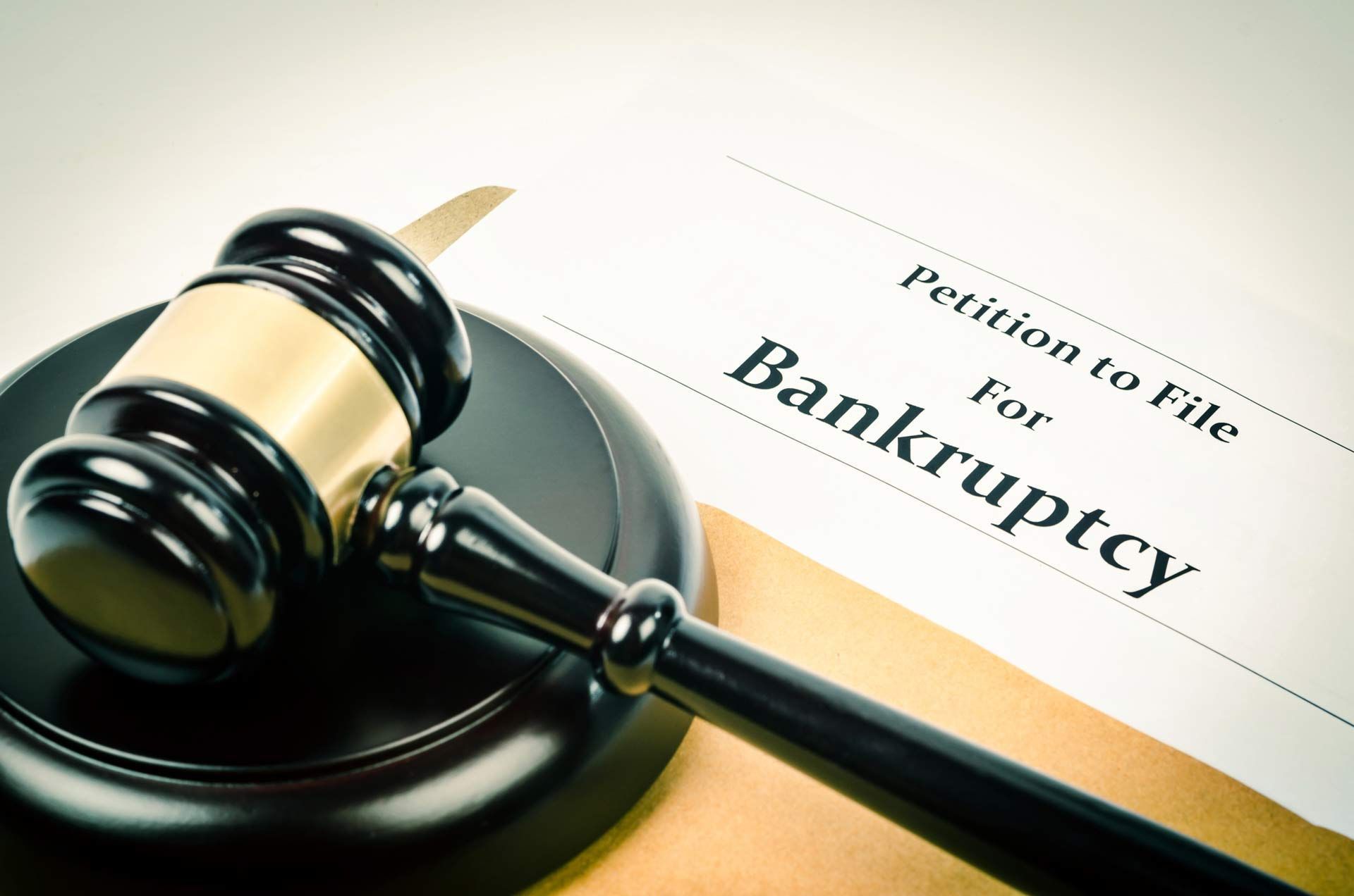 Close-up of a black wooden gavel next to a document that reads “Petition to file for bankruptcy