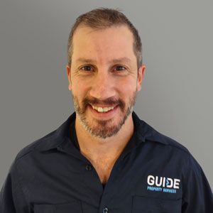 Smiling man in a navy shirt with a GUIDE logo against a gray background