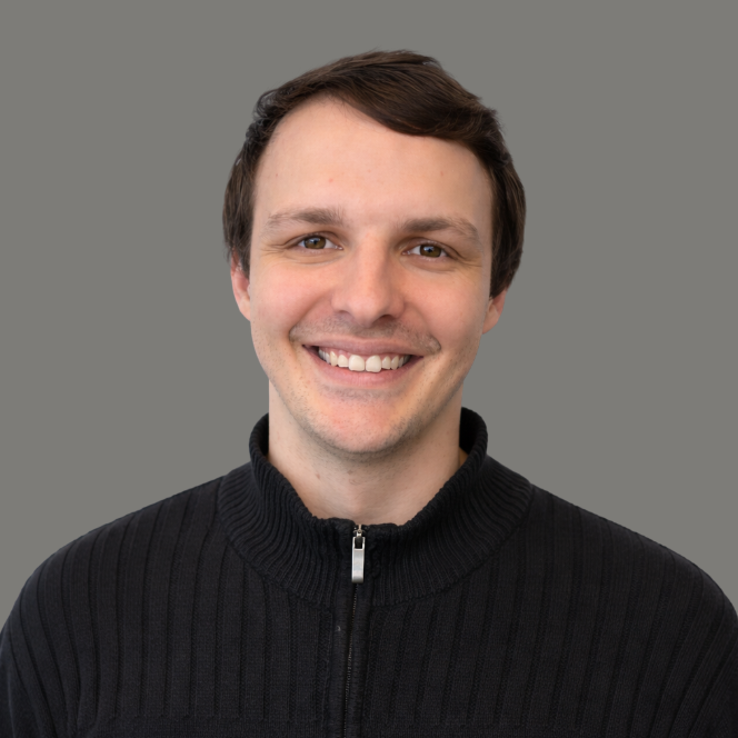 Smiling person in a plaid shirt against a plain gray background