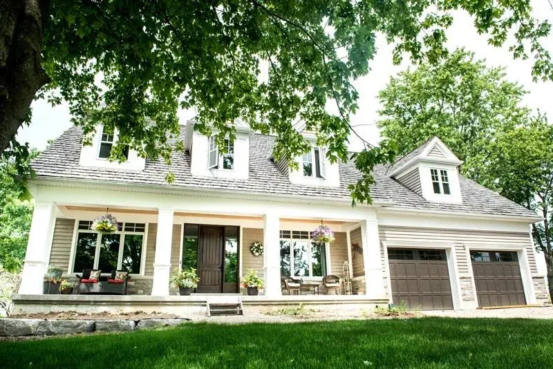 A large white house with a porch and two garages