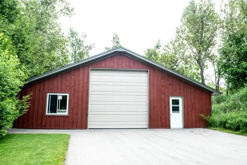 A red barn with a white garage door is surrounded by trees.