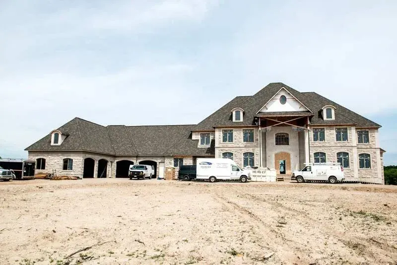 A large house is being built in the middle of a dirt field.