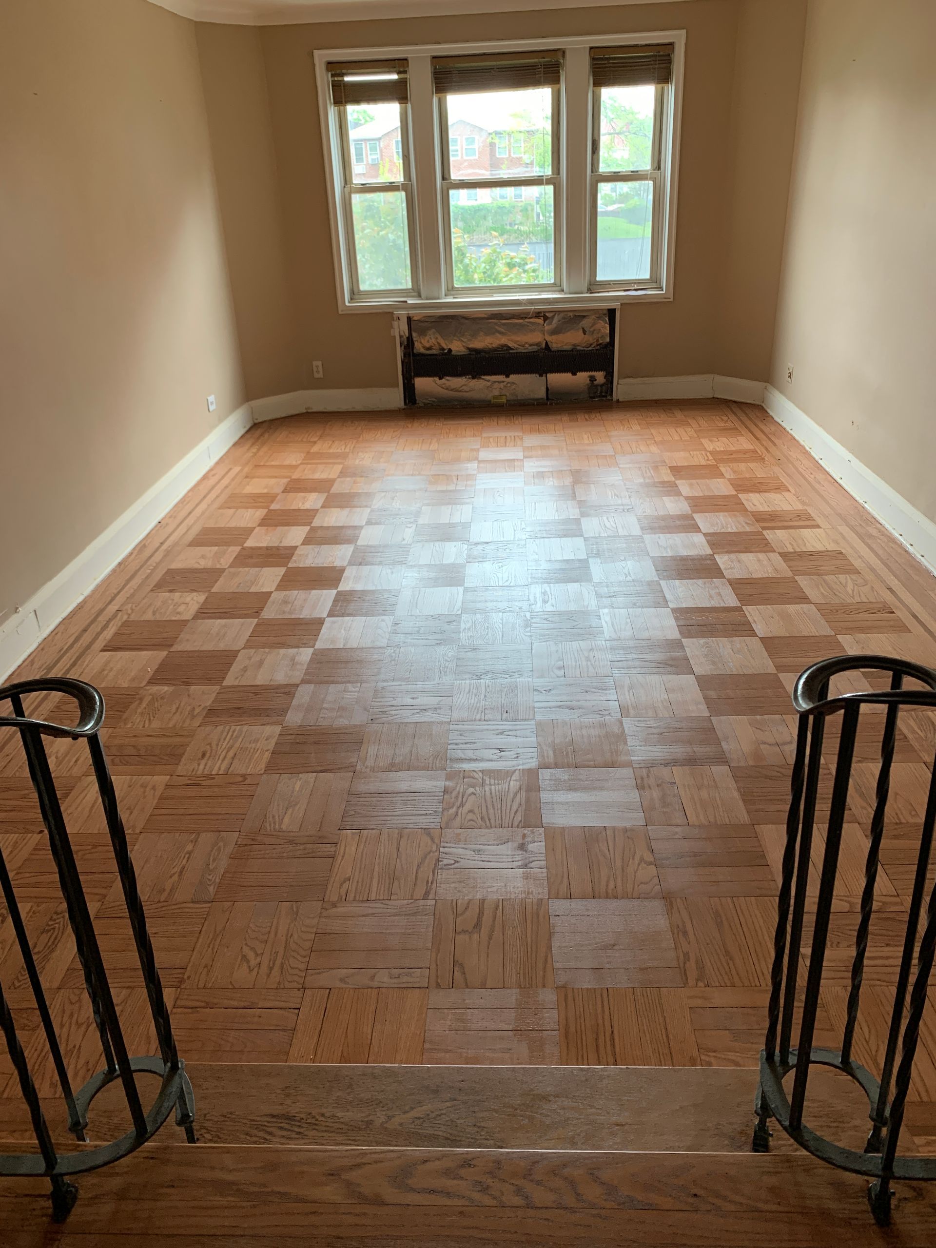 Empty room with checkered wooden floor, window, and metal railing.