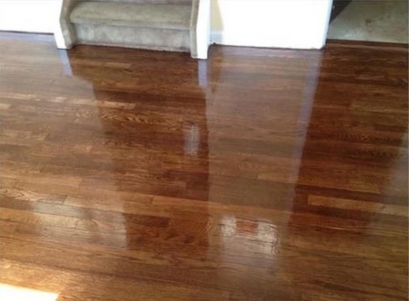Shiny, dark brown hardwood floor reflecting light, with a portion of a staircase in the background.