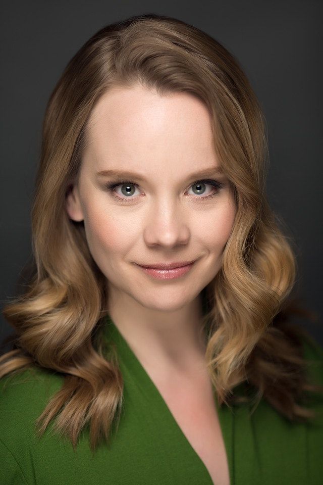 Portrait of a smiling woman with wavy blonde hair wearing a green top against a dark background