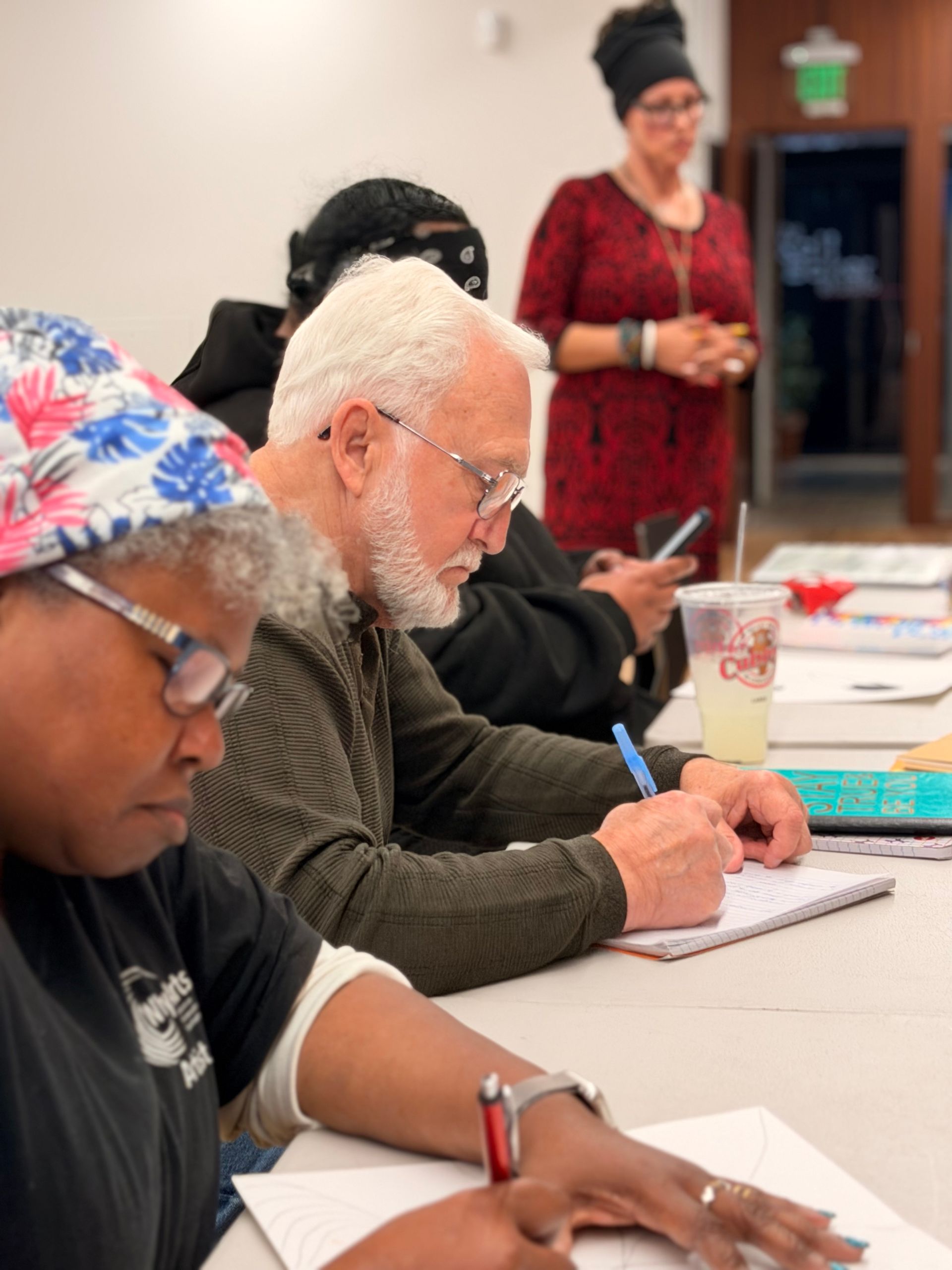 People seated at a table writing in notebooks during a class or workshop