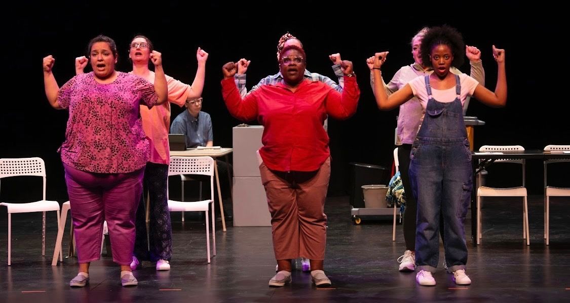 Three dancers pose on a stage with arms raised, wearing red, purple, and denim outfits.