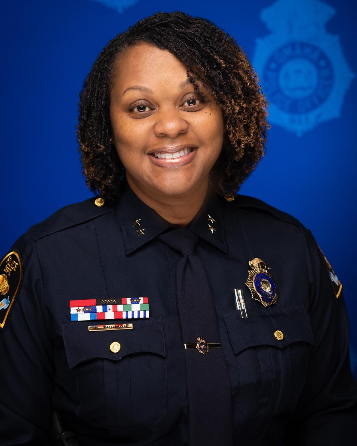 Police officer in dark uniform smiling against a blue studio backdrop