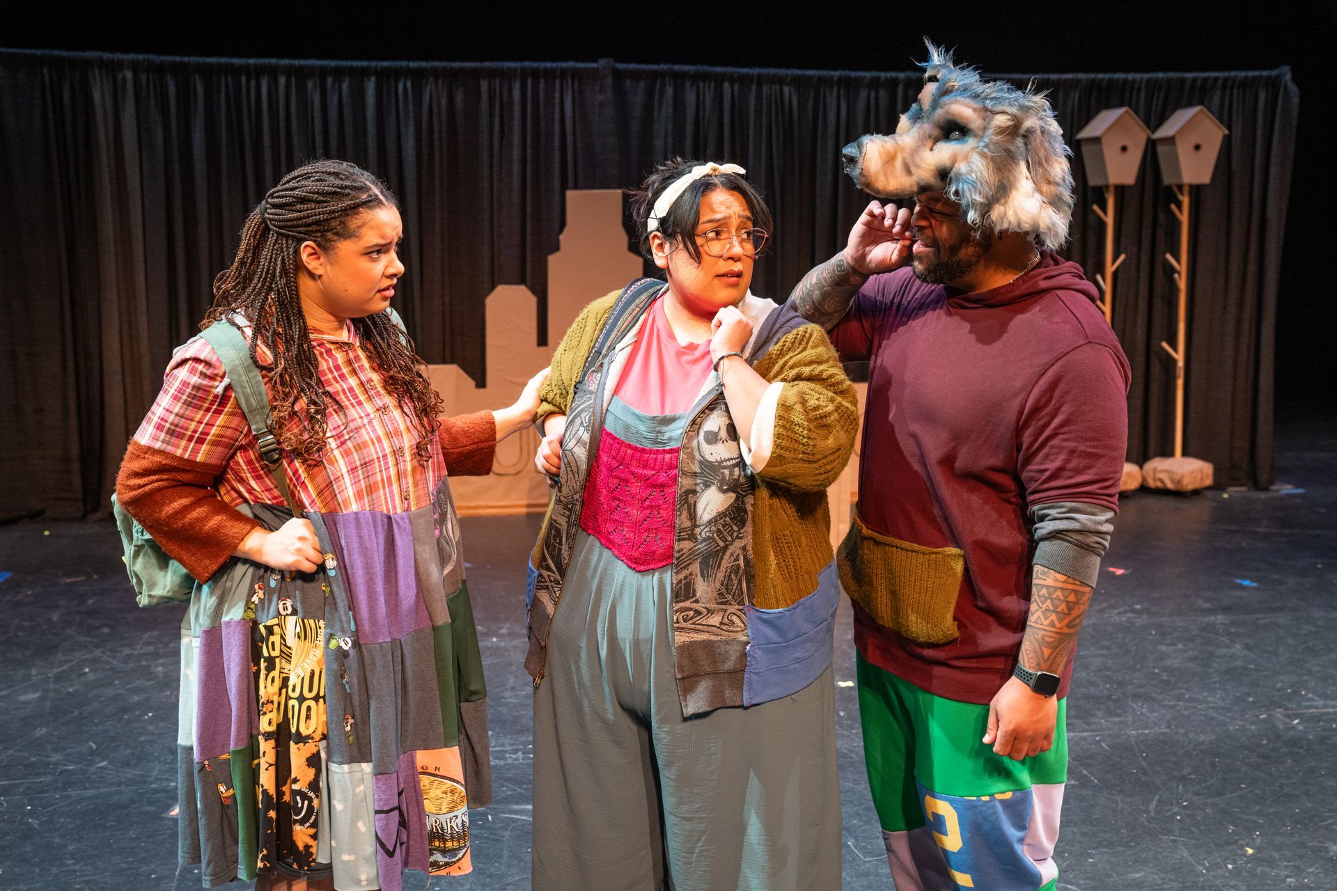 Three costumed performers on a stage, one wearing a wolf mask, in a theatrical scene