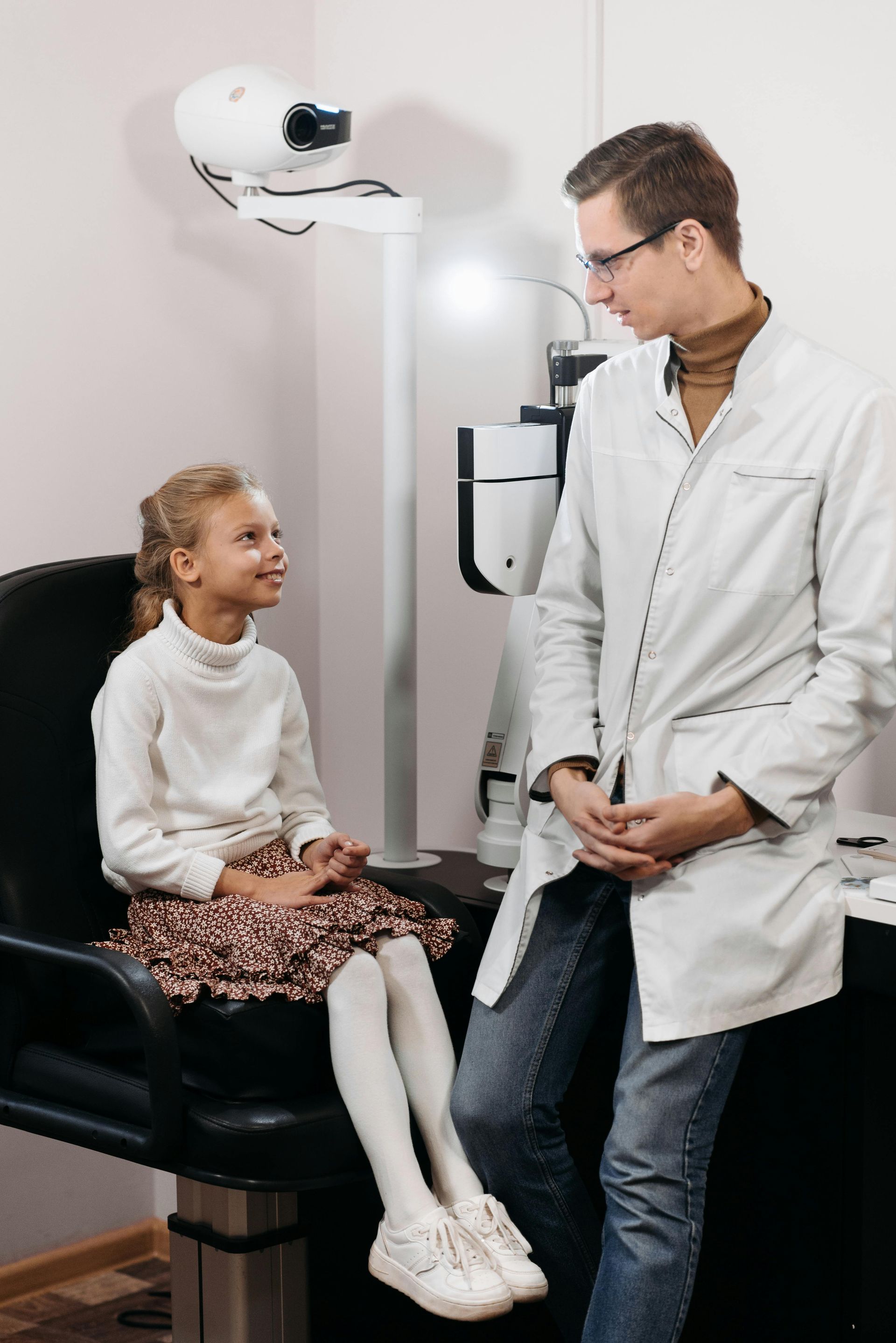 Girl sitting for an eye exam, looking at doctor in white coat.