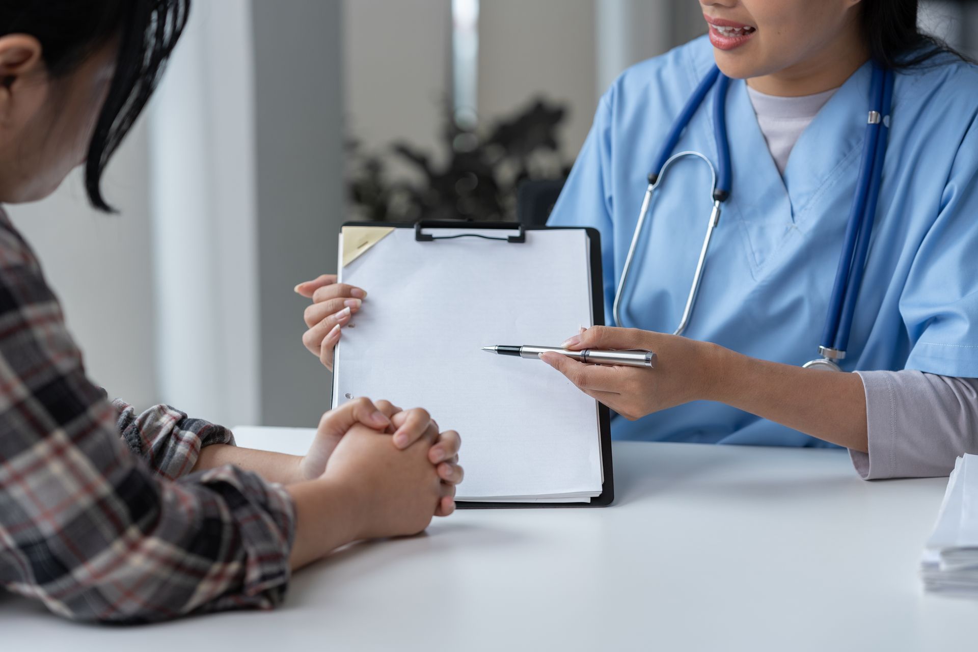 Doctor pointing to a clipboard while talking to a patient in a doctor's office.