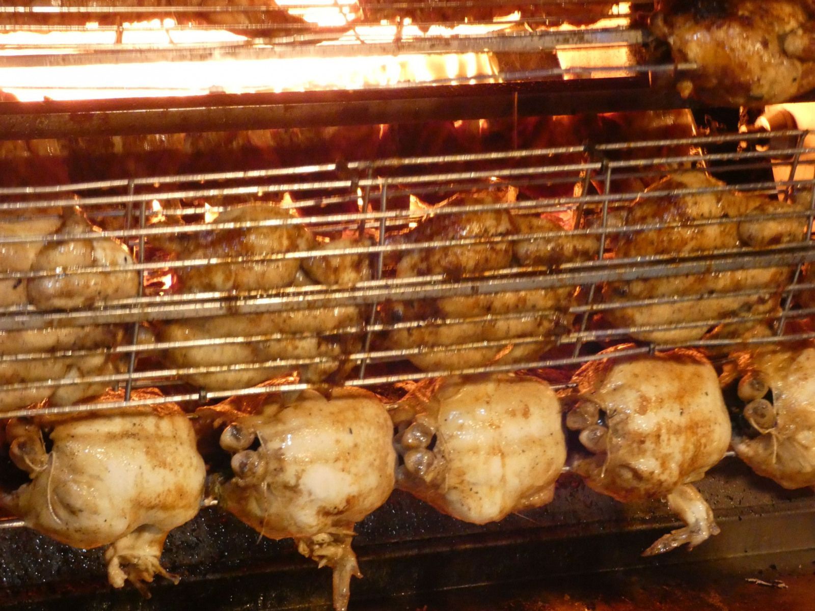 Polli interi arrostiti su una griglia metallica da girarrosto sopra una fiamma libera.