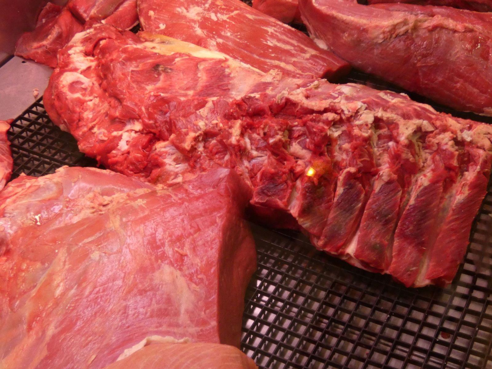 Tagli di carne rossa cruda esposti su una griglia metallica in un banco frigo di un supermercato.