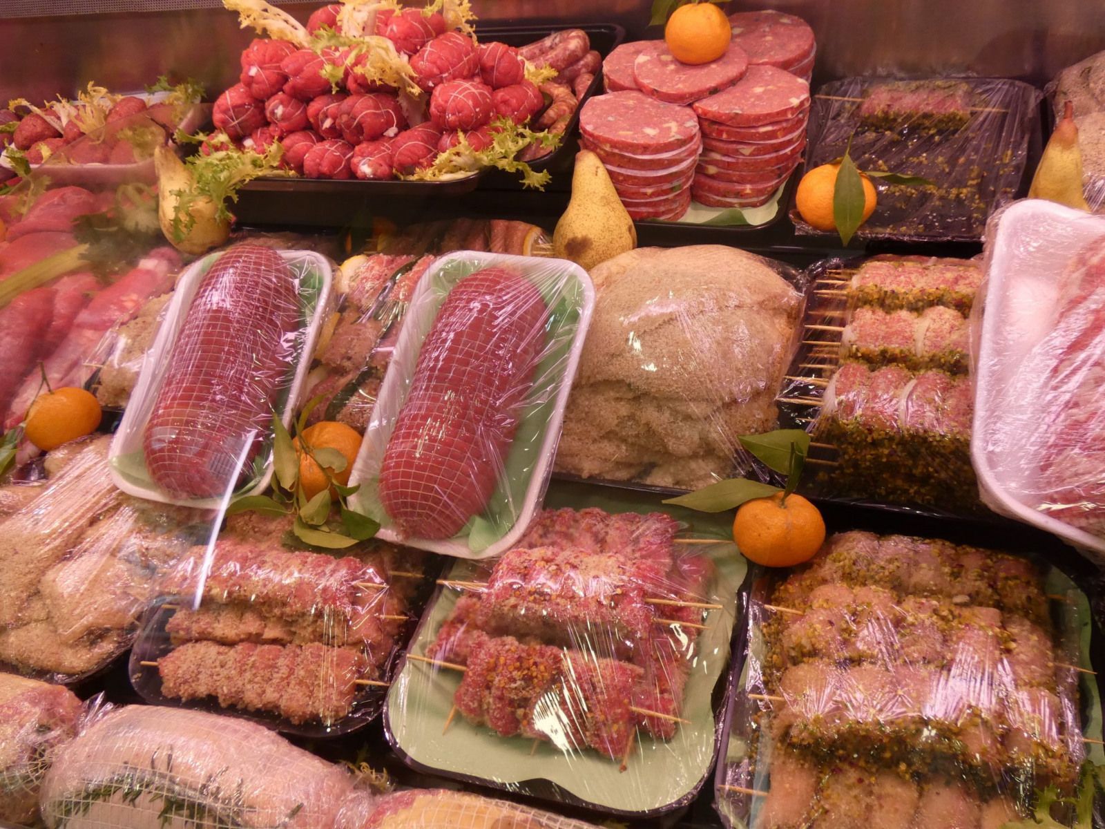 Una vetrina che espone diverse carni crude, tra cui salsicce, arrosti e spiedini, guarnite con agrumi.