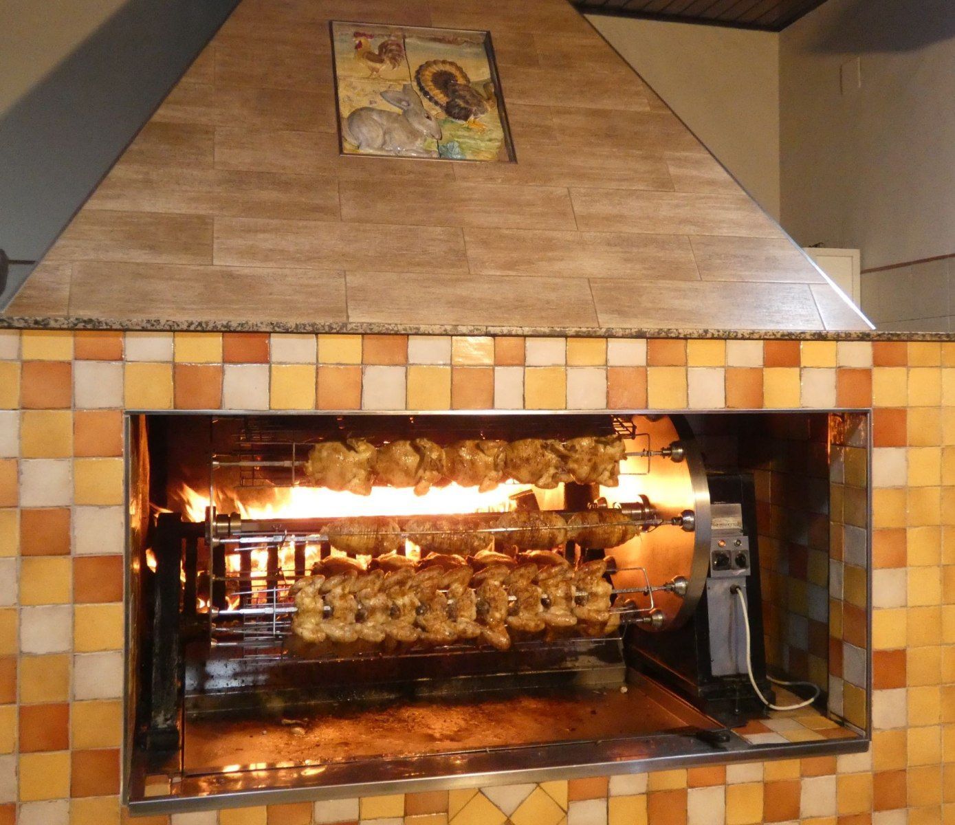 Un girarrosto all'interno di un camino piastrellato con numerosi polli che arrostiscono sul fuoco.