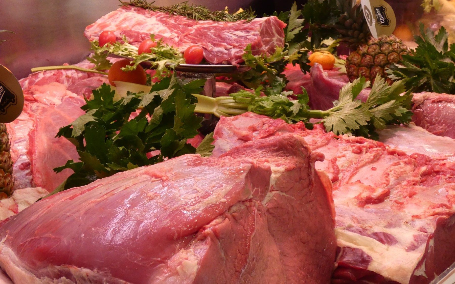 Una vetrina che espone vari tagli di carne cruda, guarniti con erbe aromatiche fresche e pomodori.